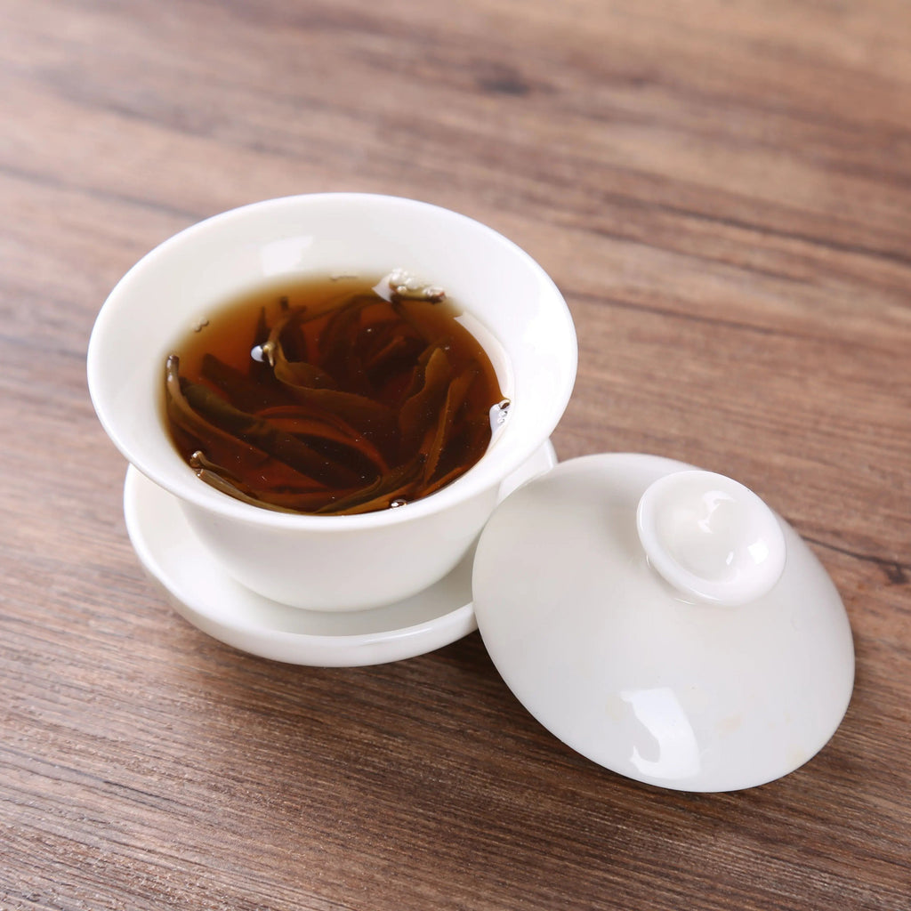 White porcelain gaiwan with brewed tea, lid placed beside it